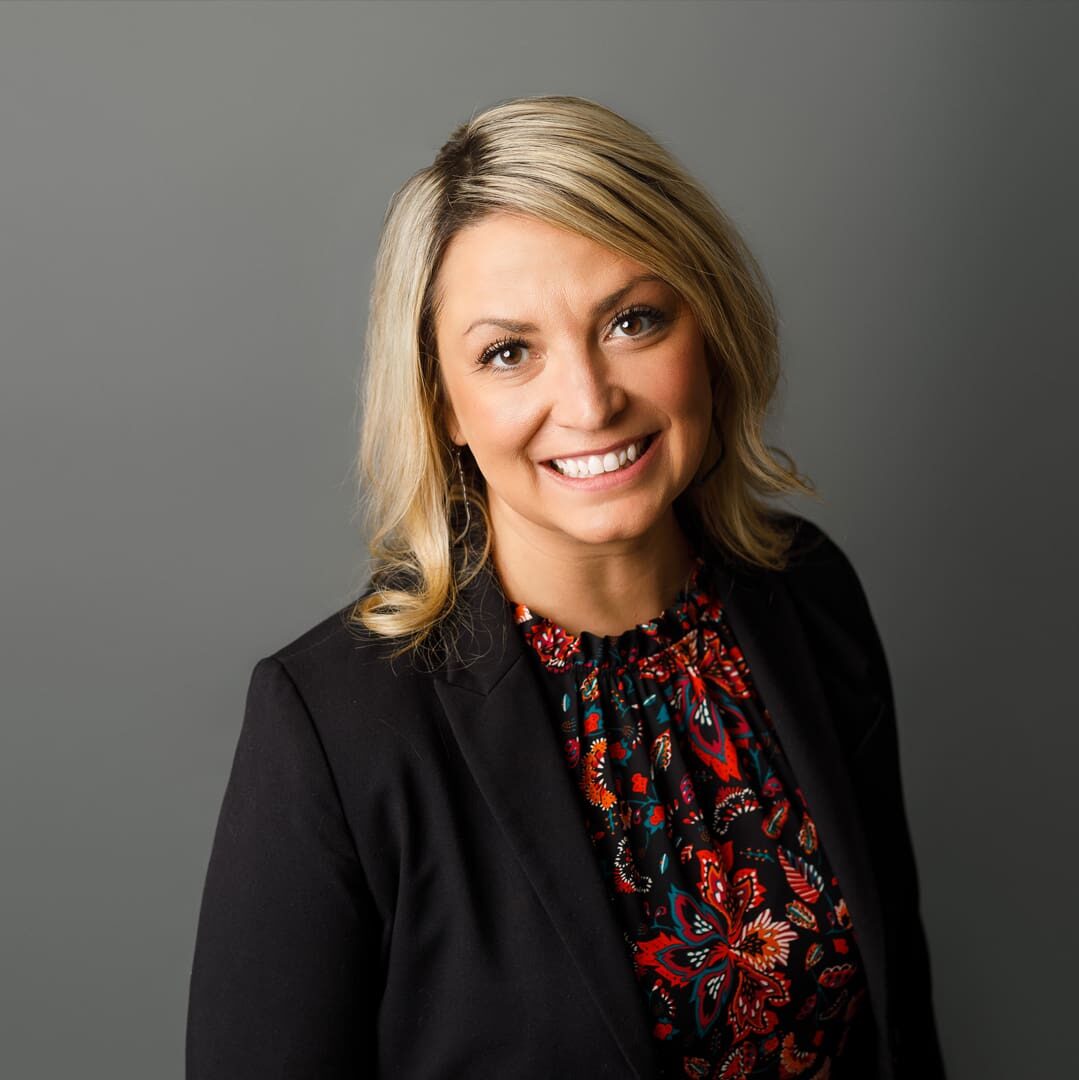A woman in black jacket and red shirt smiling.